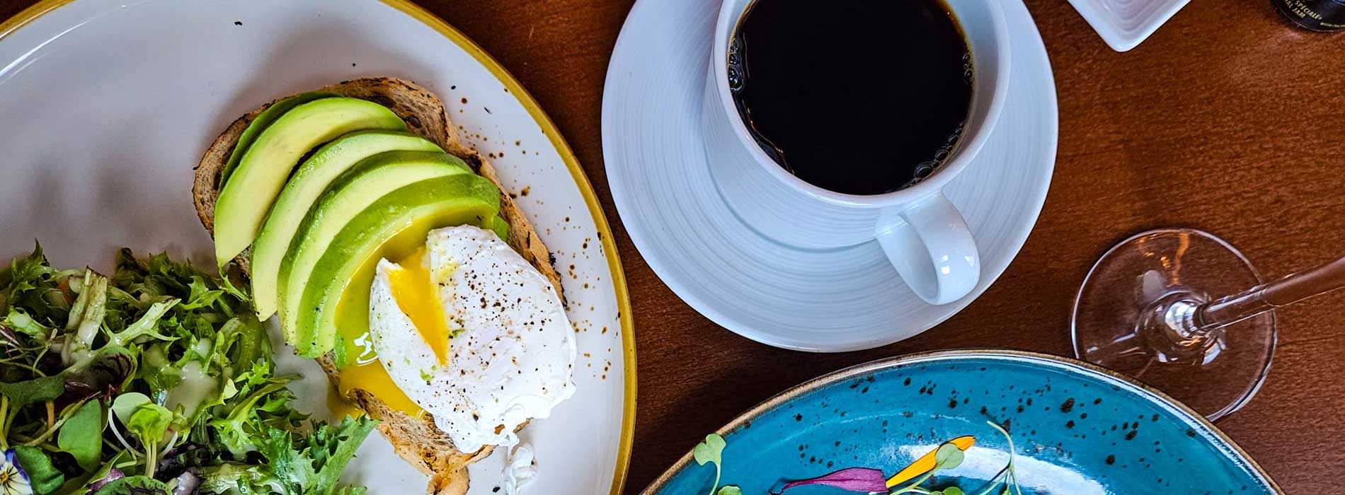 Brunch dish with salad, avocado toas with an egg, and coffee